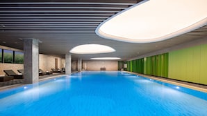 Una piscina con pavimento in piastrelle blu, circondata da sdraio e un muro verde.