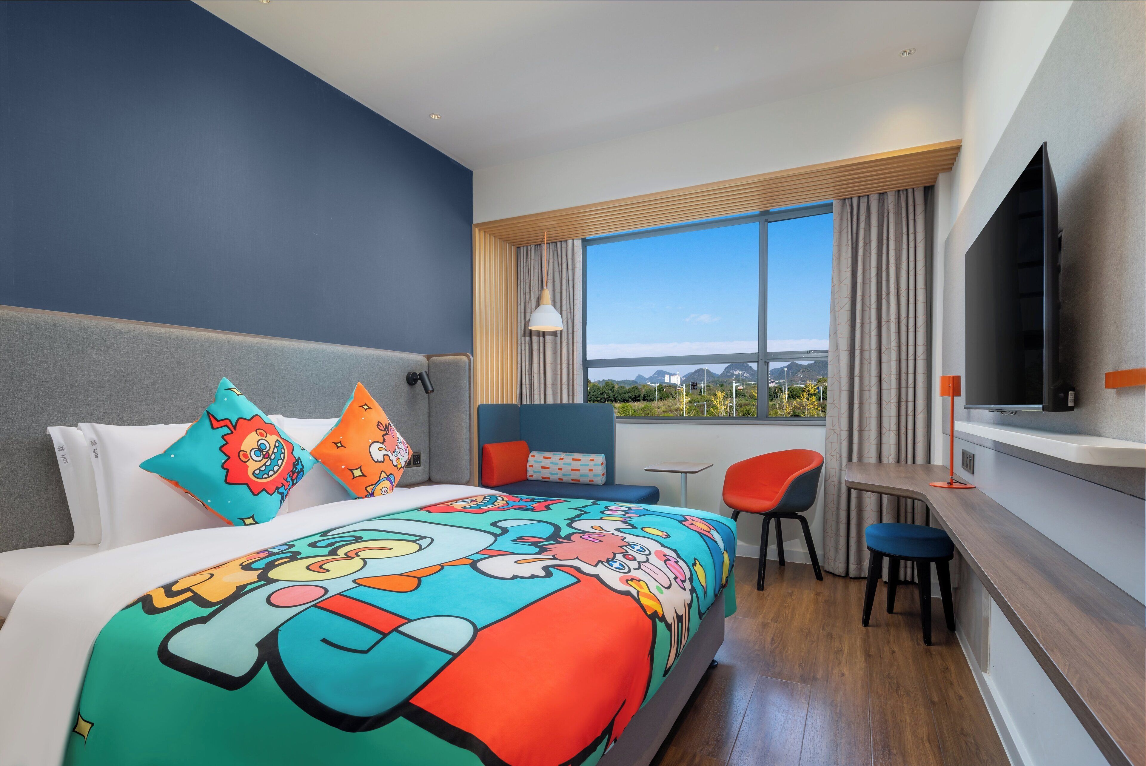 A hotel room with a large bed, a desk, a chair, a TV, and a window with a view of the city.