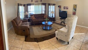 Relax in this cozy living space with a comfortable sofa, armchair, and coffee table, perfect for unwinding with a TV and a view.