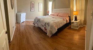Cozy retreat with a large bed, bedside table, and dresser, surrounded by framed artwork.