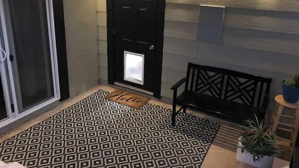 Un couloir avec un tapis à motifs, un banc, une porte avec une fenêtre et des lampes fixées au mur.