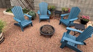 Un espace patio aménagé avec quatre chaises Adirondack bleues disposées autour d’un foyer central.