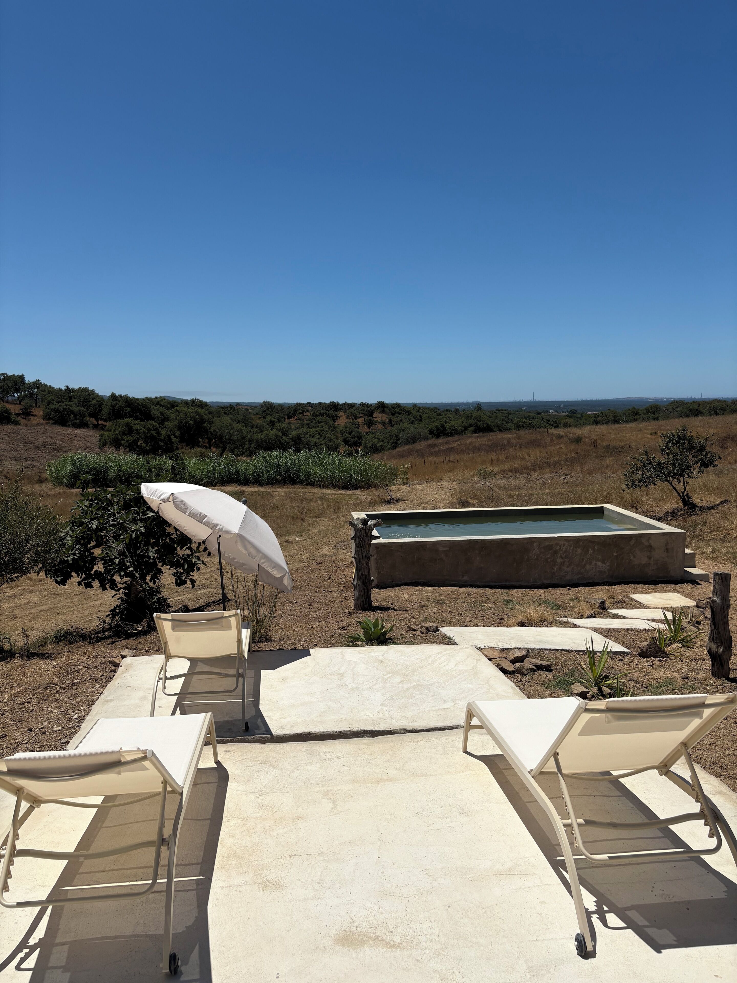 Um pátio externo com cadeiras de lounge, piscina e vista para a paisagem.
