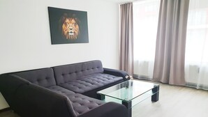 En stue med en mørk sofa, et glasbord og et billede af en løve på væggen.
