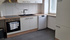 Et moderne køkken med hvide skabe, et rustfrit stål emfang, en opvaskemaskine og et vindue med naturligt lys.