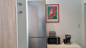 Et lille køkken med et stålkøleskab, en mikroovn og en kaffemaskine på et lille bord.