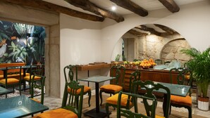 A restaurant with wooden beams, green chairs, and orange cushions. Tables are set with fruit and glassware. - Almadina Smart Luxury (Porto)