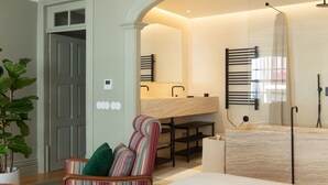 A modern bathroom with a large mirror, a sink, and a shower. There is a chair with colorful stripes and a small table with a book. - Almadina Smart Luxury (Porto)