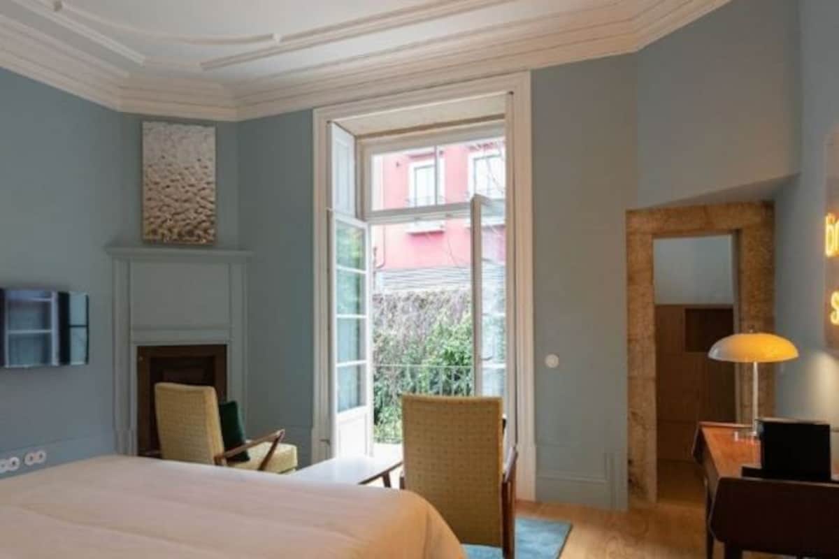 Habitación de hotel con cama, chimenea, sillón, escritorio y vistas al exterior.