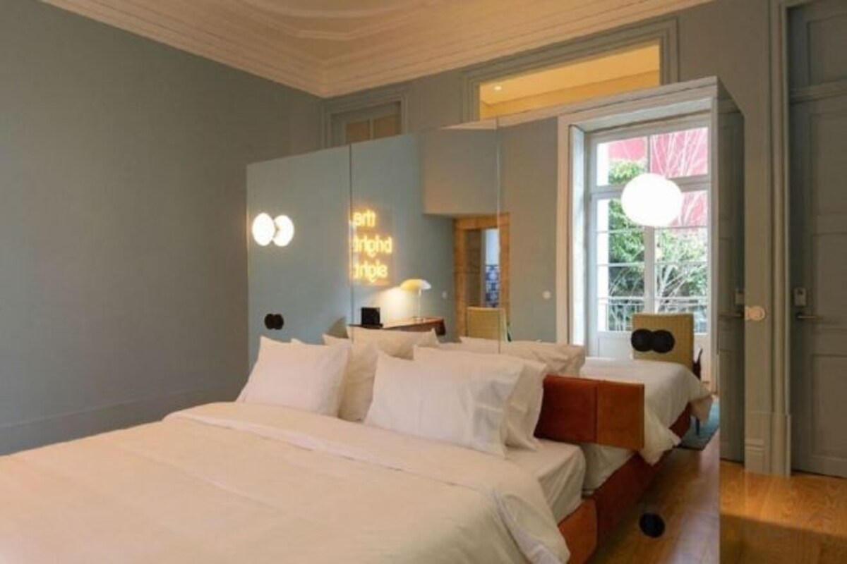 A bedroom with a large bed, a bedside table, a lamp, and a window with a view.