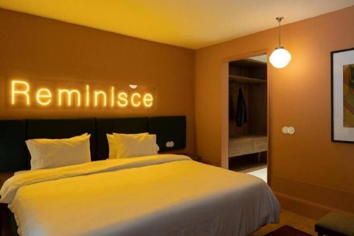 Hotellihuone, jossa on sänky, sängynpääty, seinälle kiinnitetty kyltti, vaatekaappi ja riippuvalaisin.