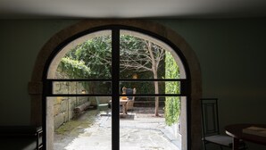 A room with a large arched window overlooking a courtyard with a stone wall, a wooden table, and a chair. - Almadina Smart Luxury (Porto)