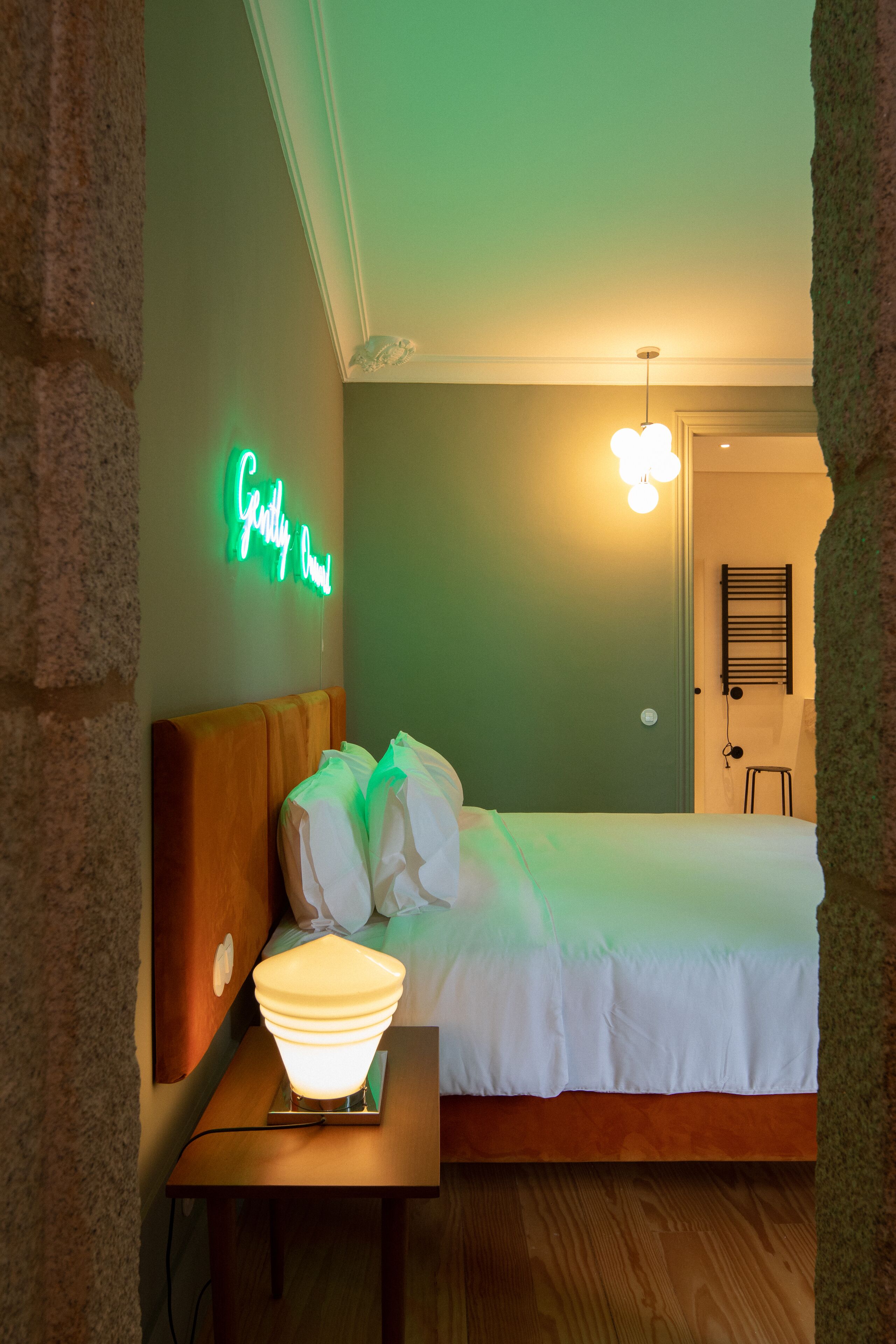 A neatly made bed with a headboard, a bedside lamp, and a neon sign on the wall.