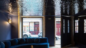 A modern interior with a curved blue sofa, a round black table with a bottle, and a view of the street outside. - Almadina Smart Luxury (Porto)