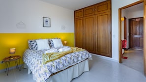 A bedroom with a bed, a wooden wardrobe, and a small bedside table. - Sun House by LovelyStay (Olhos de Água)