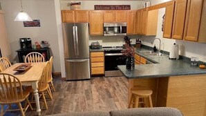 A compact kitchen with wooden cabinets, a stainless steel refrigerator, a microwave, and a sink. - Beautiful Lake View - Townhome (Saint Germain)
