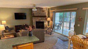 A living room with a stone fireplace, a sofa, a coffee table, and a dining area with wooden chairs. - Beautiful Lake View - Townhome (Saint Germain)