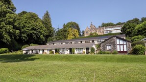 Un grand bâtiment à plusieurs étages, de style architectural traditionnel, entouré d’une végétation luxuriante et d’une pelouse bien entretenue.
