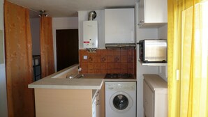 Een functionele keuken met een wasmachine, een magnetron en een gasfornuis.