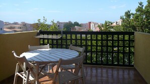 Een balkon met een tafel, stoelen, een barbecue en uitzicht op de stad.