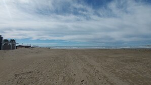 Een breed zandstrand met voetafdrukken die naar een steiger leiden.