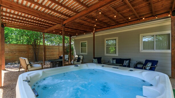 Un jacuzzi bajo un porche de madera con asientos y vista a una casa.