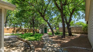 Un sendero de piedra que conduce a una pequeña casa verde en un patio trasero con árboles y una valla.