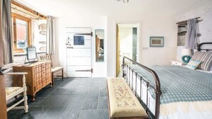 A bedroom with a bed, a dresser, a bench, and a door leading to another room. - St Davids Hideaway with Roll-top Bath & Log Burner (St Davids)