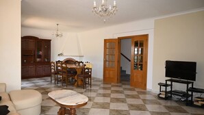 Una sala de estar con una mesa de comedor, sillas, un sofá, un televisor y una araña.