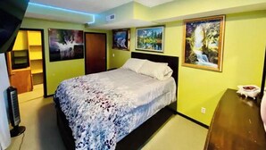 Ein Schlafzimmer mit einem Bett, einer Kommode, einem an der Wand montierten Fernseher und einer Tür zu einem Badezimmer.