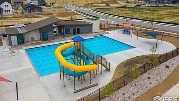A swimming pool with a slide, surrounded by a paved deck and a fence. - Modern Comforts: 3-Bedroom Townhome w/ 2 kid friendly community pools 
 (Fort Collins)