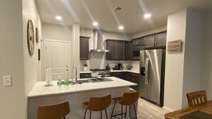 A modern kitchen with a central island, stainless steel appliances, and wooden bar stools. - Modern Comforts: 3-Bedroom Townhome w/ 2 kid friendly community pools 
 (Fort Collins)