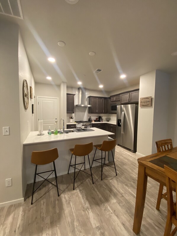 A modern kitchen with a central island, stainless steel appliances, and wooden bar stools.