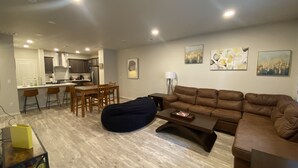 A modern living room with a brown leather sofa, a coffee table, and a bean bag. There is a dining area with a table and chairs, and a kitchen in the background. - Modern Comforts: 3-Bedroom Townhome w/ 2 kid friendly community pools 
 (Fort Collins)