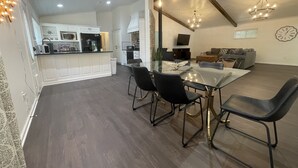 Un vaste espace de vie comprenant une table à manger, des chaises noires, un canapé gris et un téléviseur.