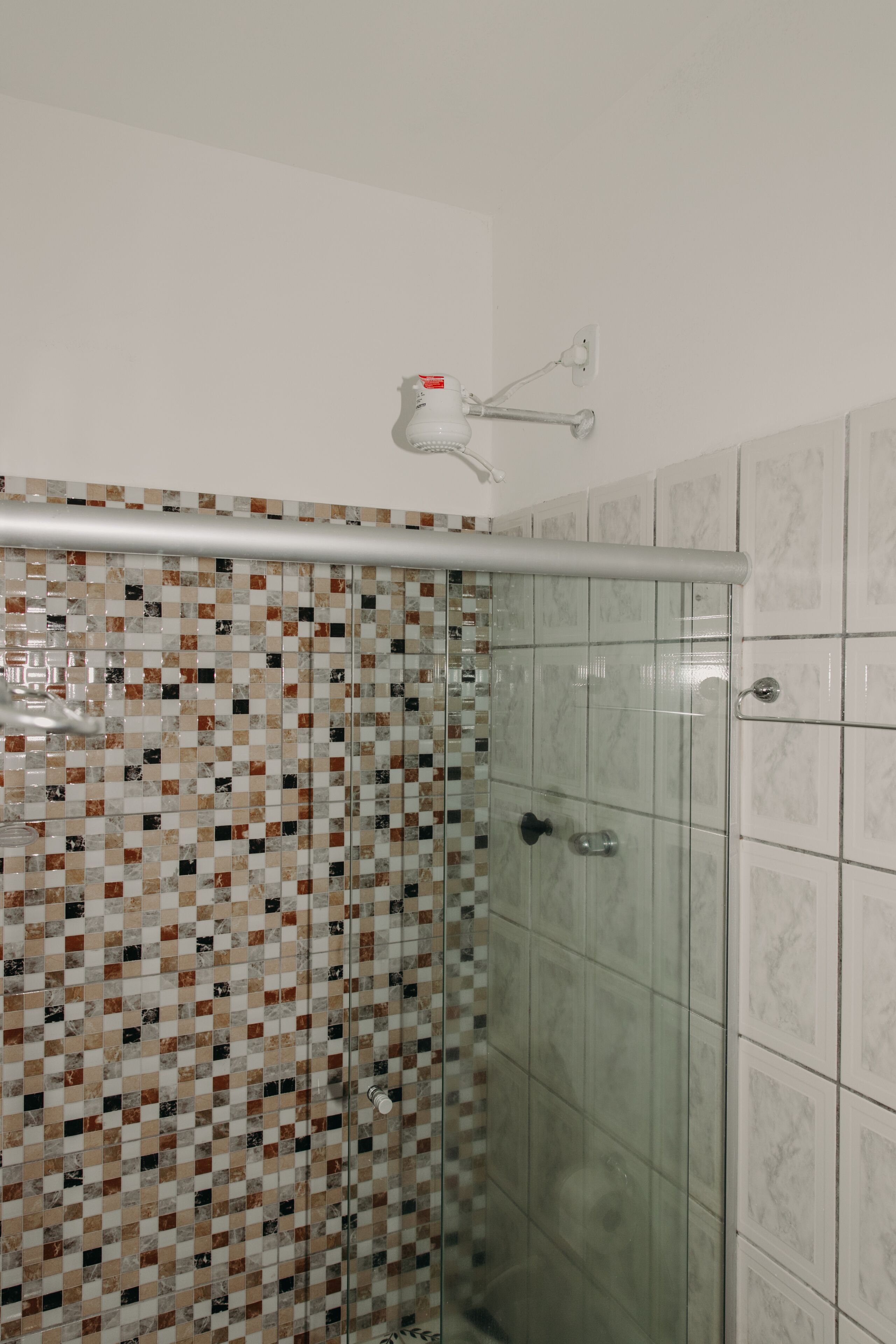 A shower area with a glass door, a tiled wall with a checkered pattern, and a white ceiling light fixture.