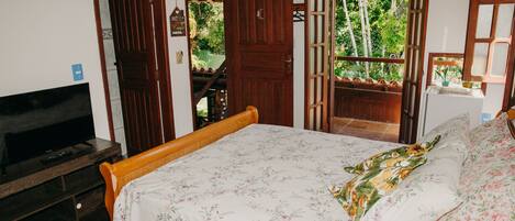 A bedroom with a bed, a TV, and a view of the outdoors through open doors.