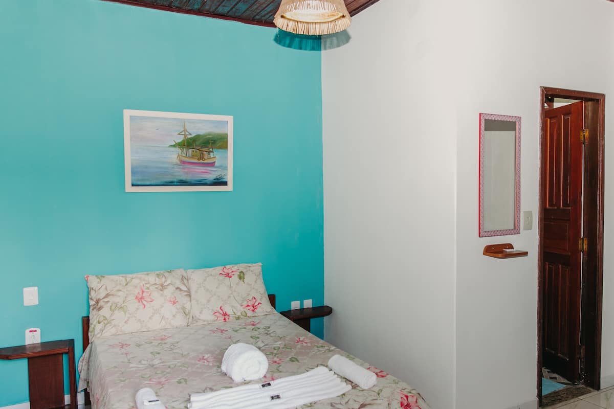 Un dormitorio con cama, un cuadro de un barco en el agua, una puerta de madera y un espejo en la pared.