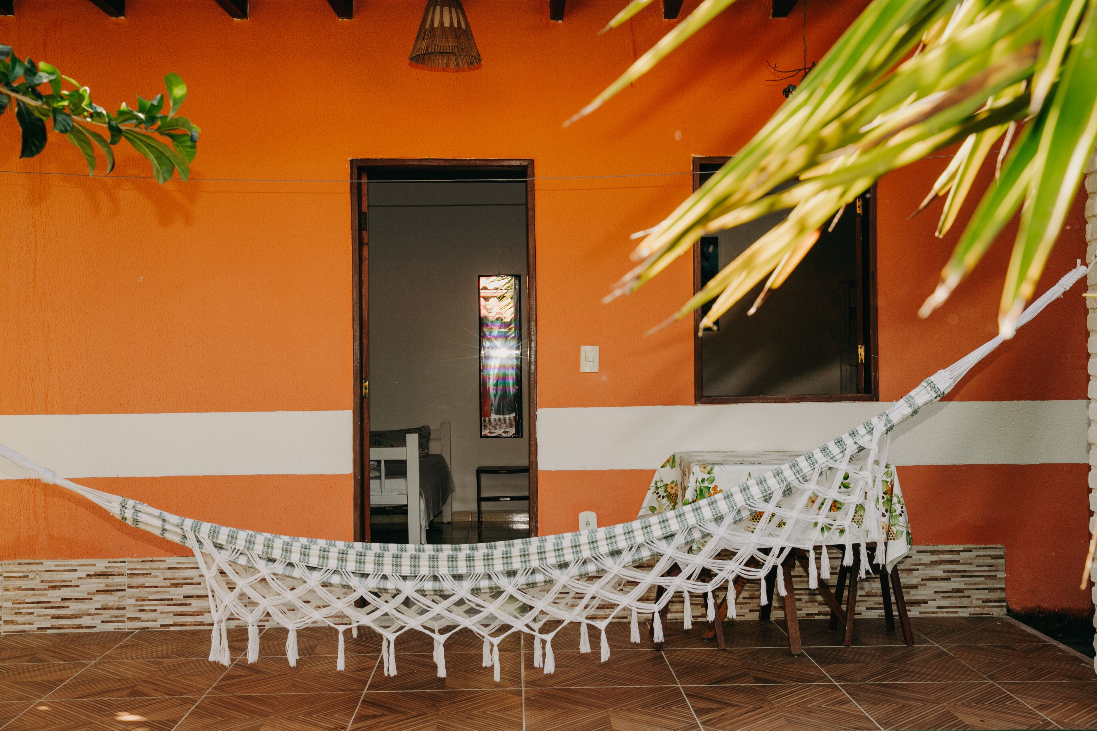 Een hangmat op een betegeld terras met een tafel, stoelen, een deur en een raam met uitzicht op het interieur.