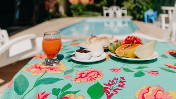Taula al costat de la piscina amb un mantell de flors, un got de suc de taronja i un plat de menjar.