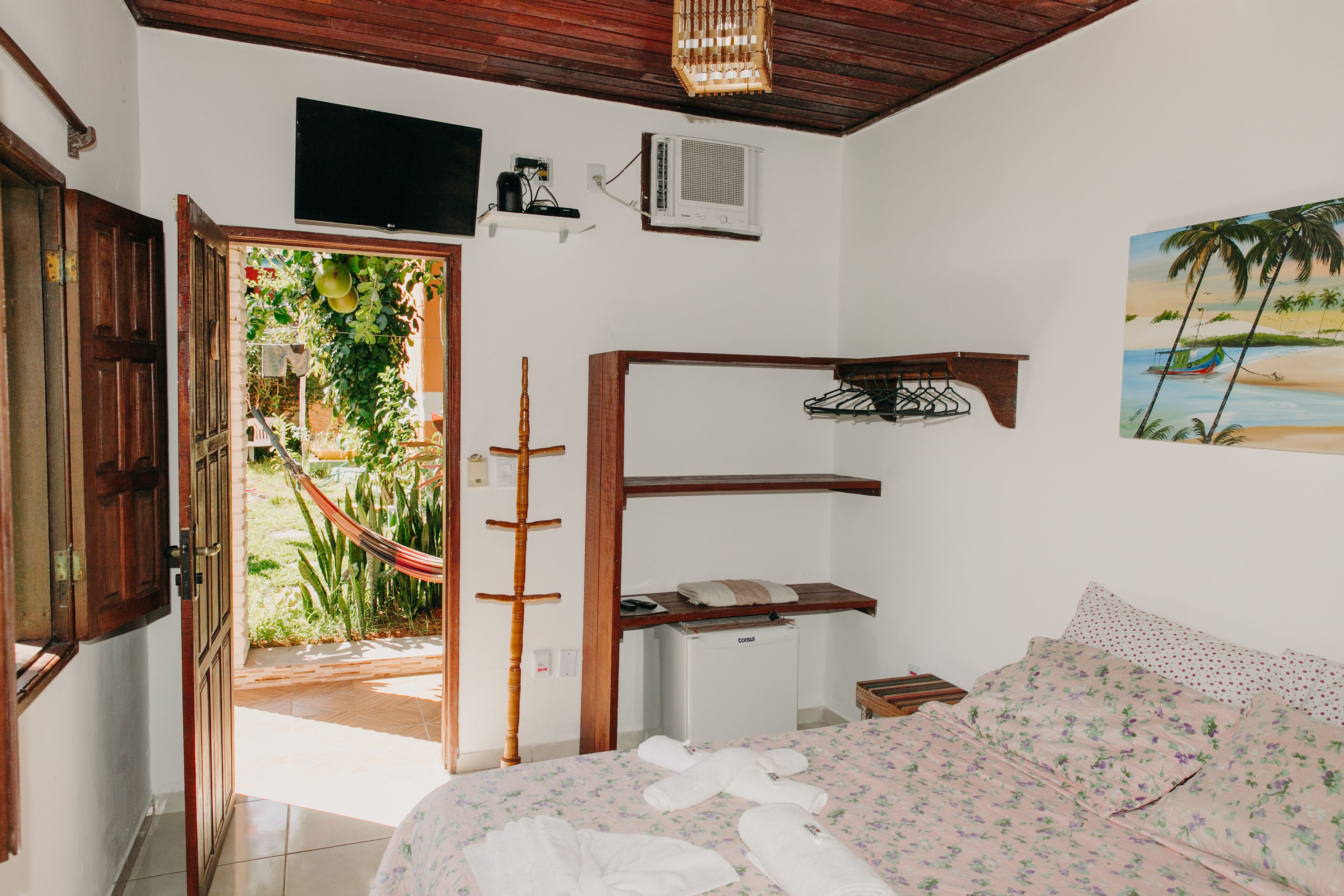 A bedroom with a bed, a TV, a small desk, and a hammock outside the door.