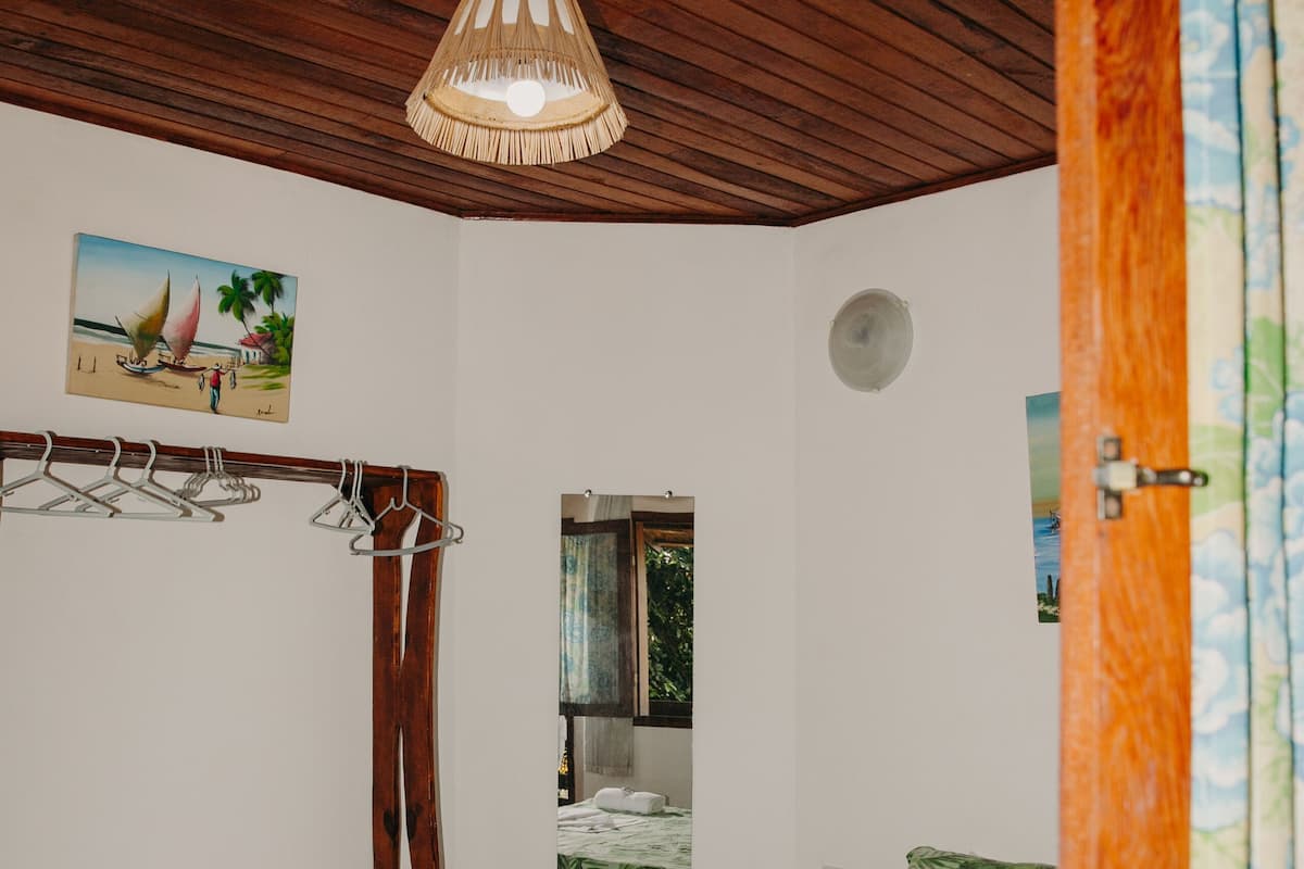 Un dormitorio con cama, una lámpara colgante, un banco de madera, un tendedero de pared y una puerta con cortina floral.