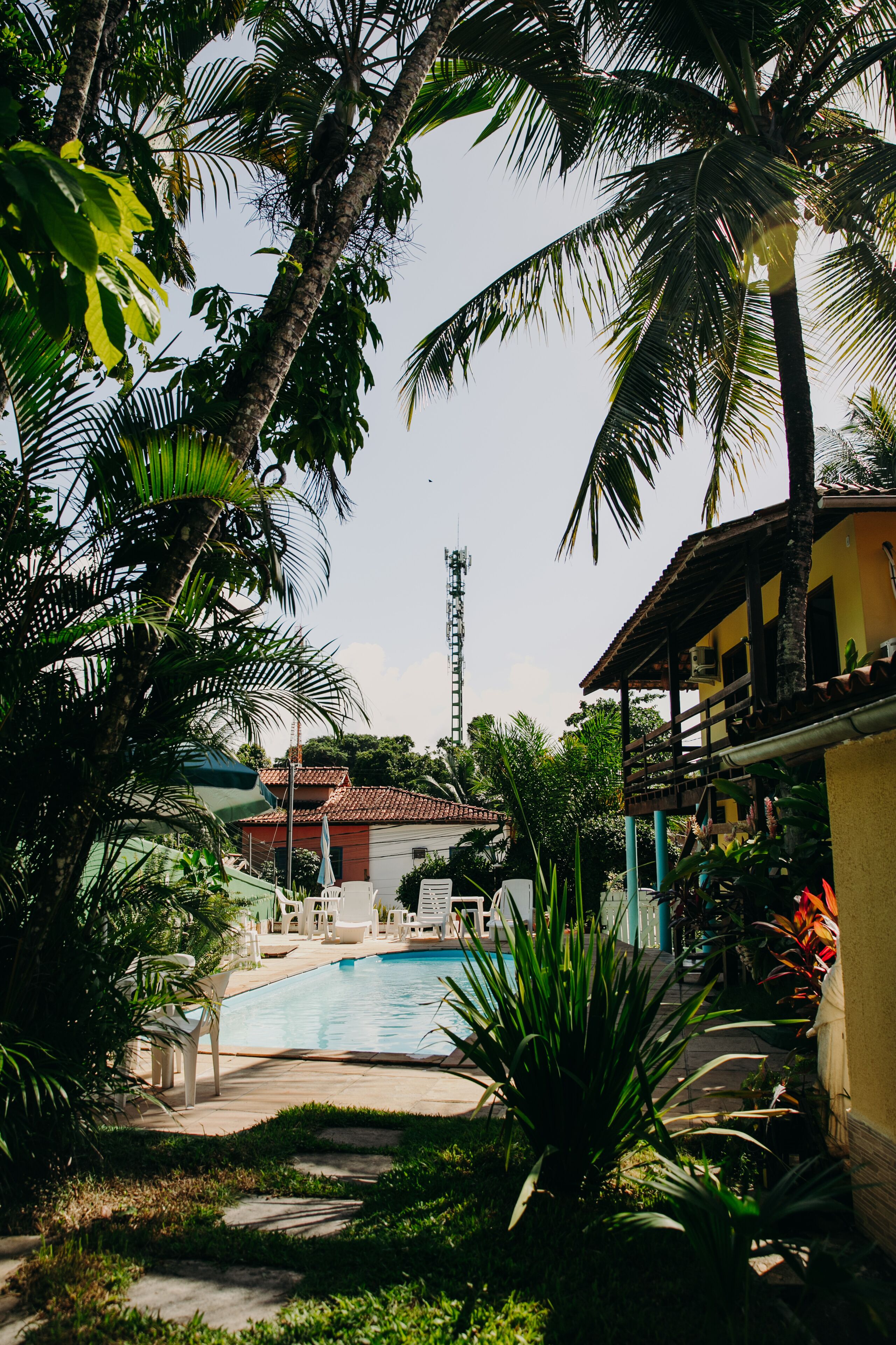 A pool area with lounge chairs, palm trees, and a building with a red roof.
