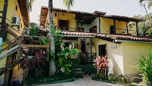 Edifici de dos pisos amb un balcó, envoltat de plantes tropicals i una escala.