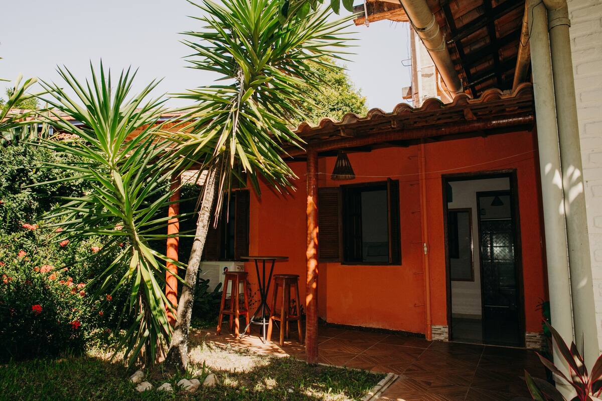 Un patio con una palmera, una mesa de madera y un edificio rojo con suelo de baldosas.