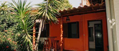 A courtyard with a palm tree, a wooden table, and a red building with a tiled floor.