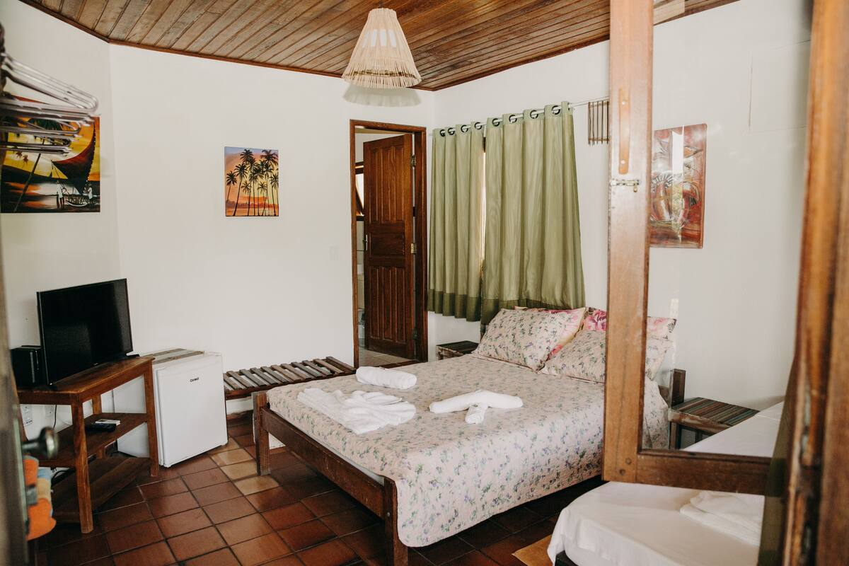 Un dormitorio con una cama, un televisor, un refrigerador pequeño y un escritorio de madera.