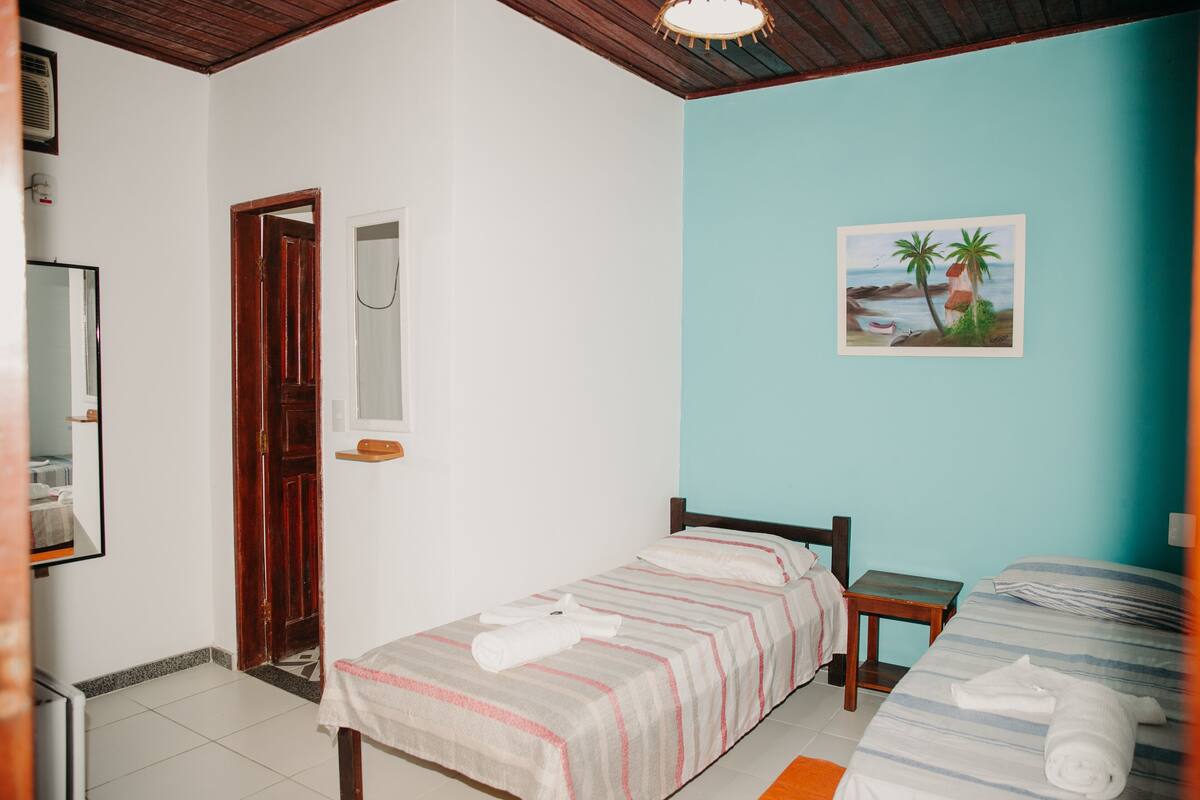 Un dormitorio con cama, mesita de noche, un cuadro de una playa y una puerta de madera.