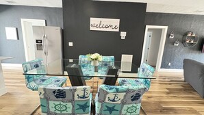 A modern living room with a glass dining table, nautical-themed chairs, a dark accent wall, and a 'welcome' sign. - EPIC Home in Heart of Miami | Near Beach & Havana (Miami)