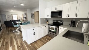A modern kitchen with white cabinets, stainless steel appliances, and a wooden floor. - EPIC Home in Heart of Miami | Near Beach & Havana (Miami)